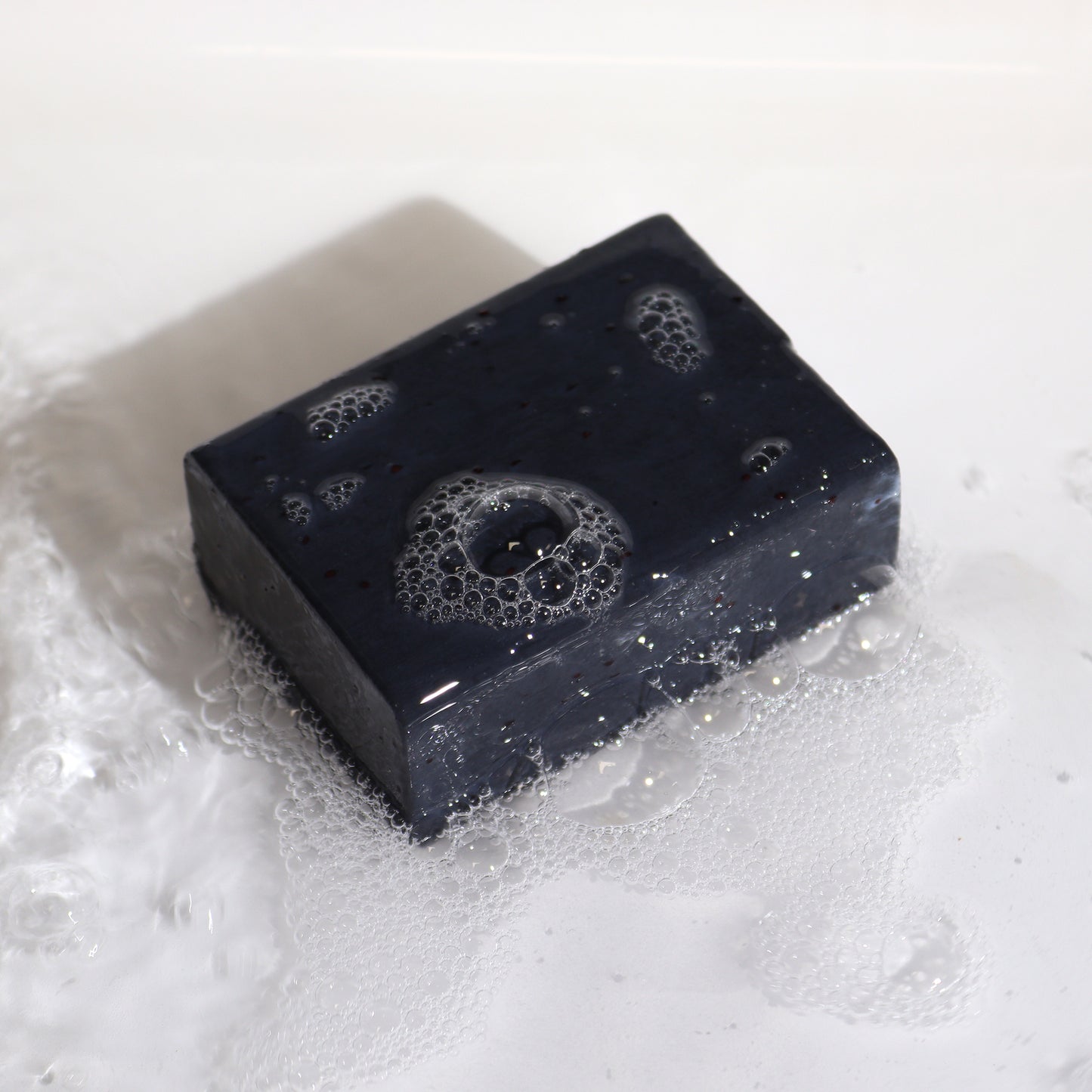 Exposed soap bar on white background with bubbles and dark charcoal glow