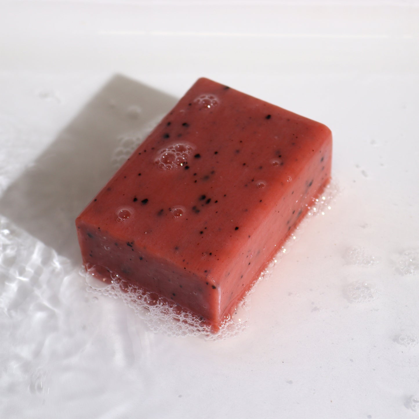 Exposed soap bar on white background with bubbles with dark charcoal bits