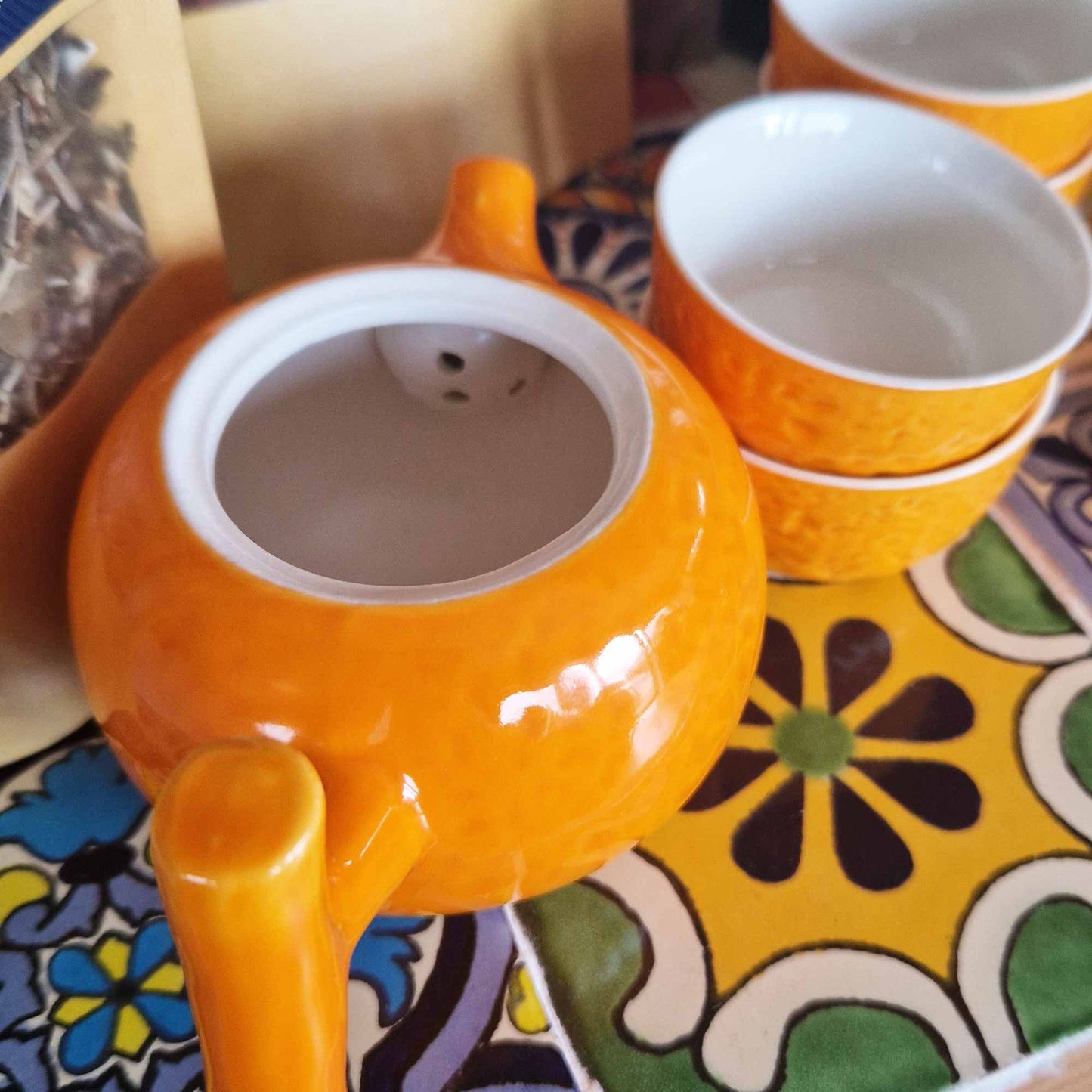Orange teapot and cups on a colorful patterned tablecloth
