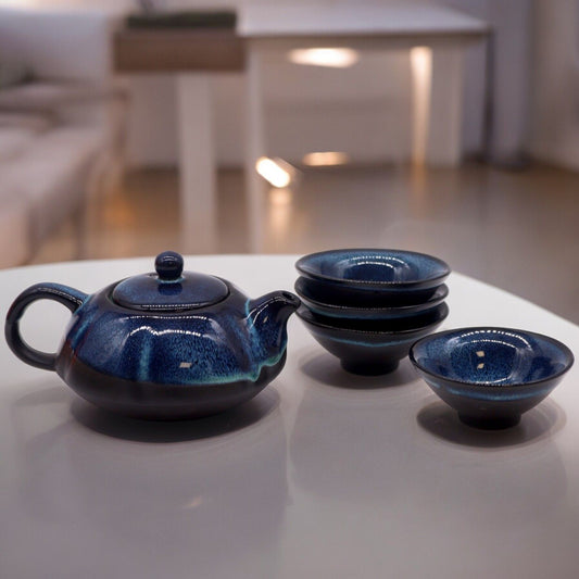Blue ceramic teapot and four bowls on a white surface with a blurred indoor background