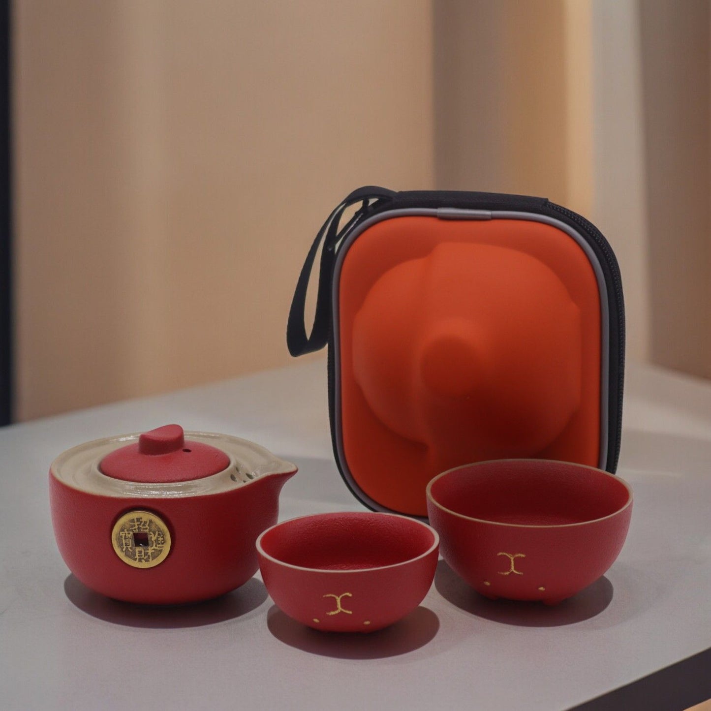 Red ceramic tea set with a carrying case on a light surface.