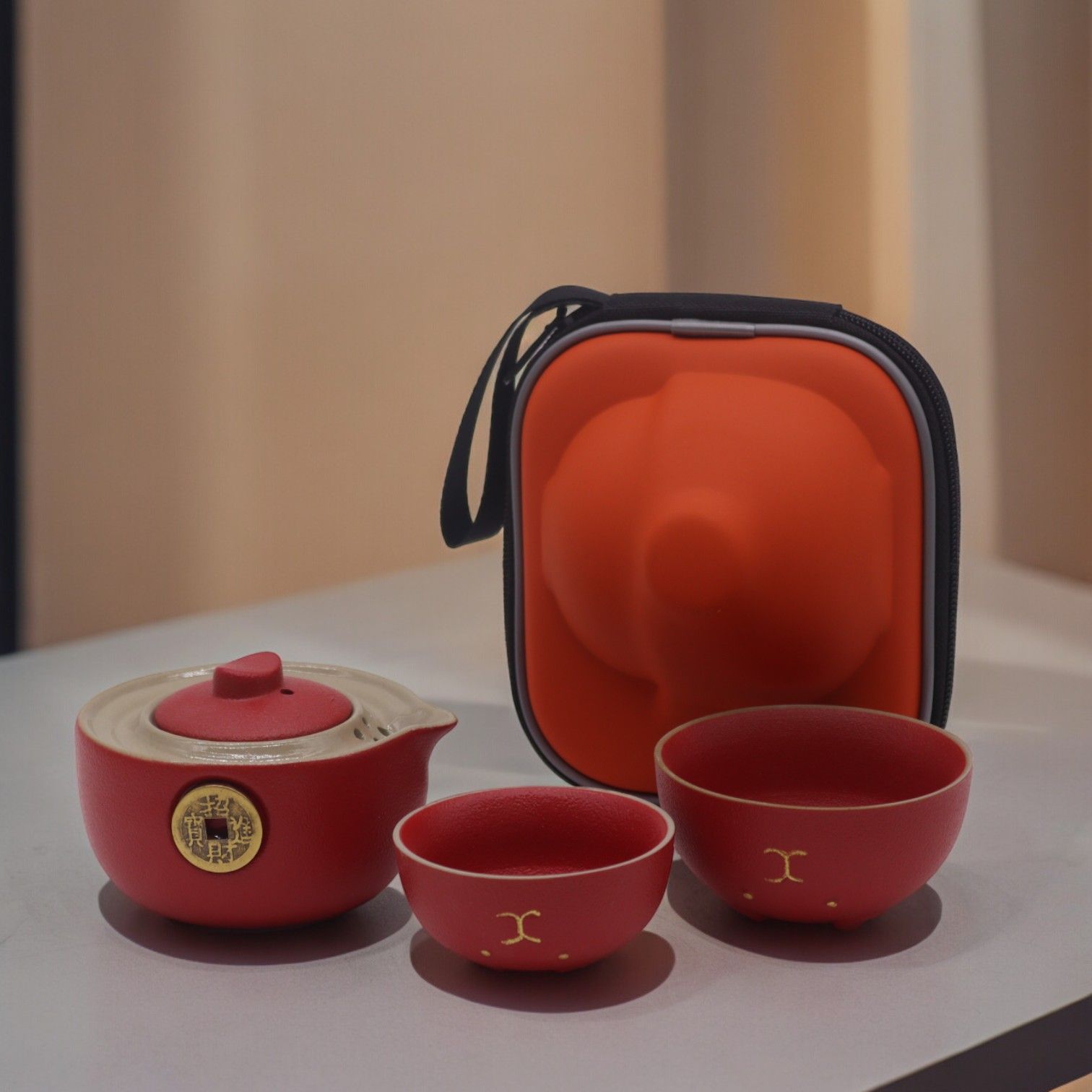 Red ceramic tea set with a carrying case on a light surface.