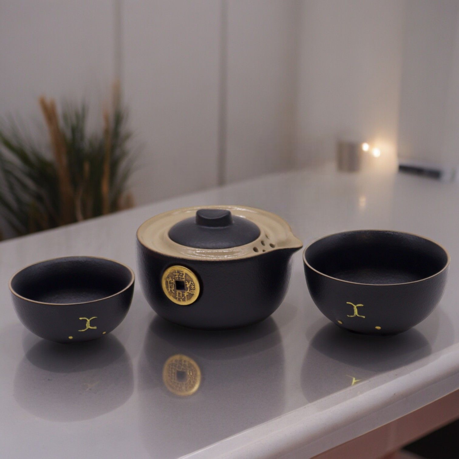 Black ceramic teapot and two bowls on a reflective surface with a blurred background