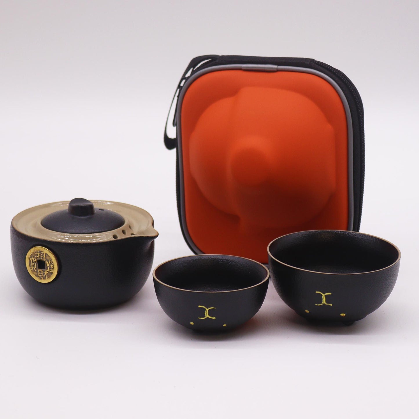 Black teapot and two black cups with a red carrying case on a white background