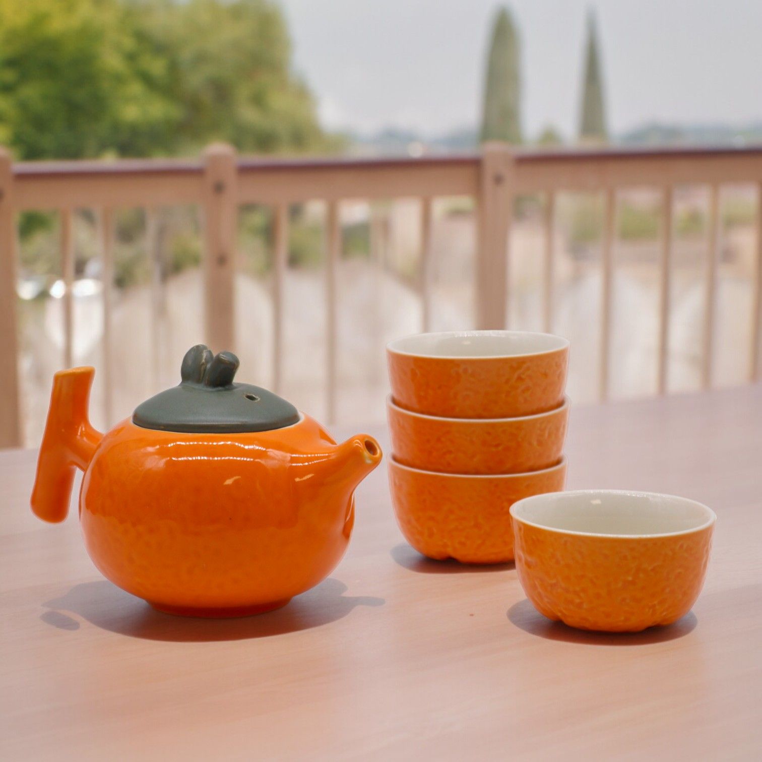Orange teapot and cups on a table with a blurred outdoor background