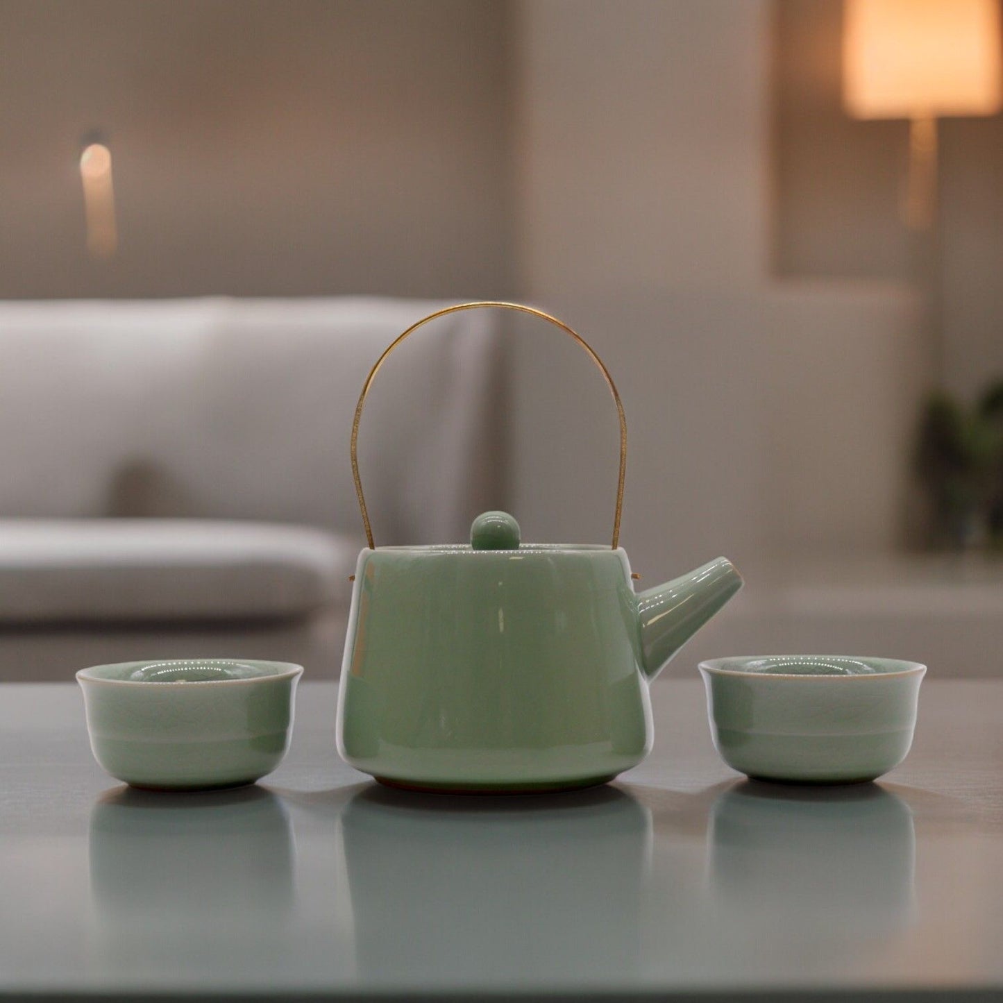 Green ceramic teapot with two matching cups on a reflective surface.