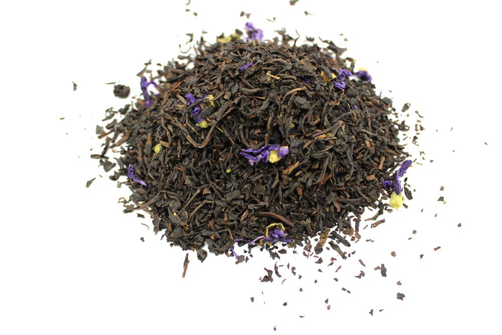 Dry black tea leaves with purple flowers on a white background