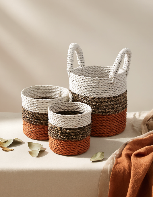 Three woven baskets with handles on a neutral background